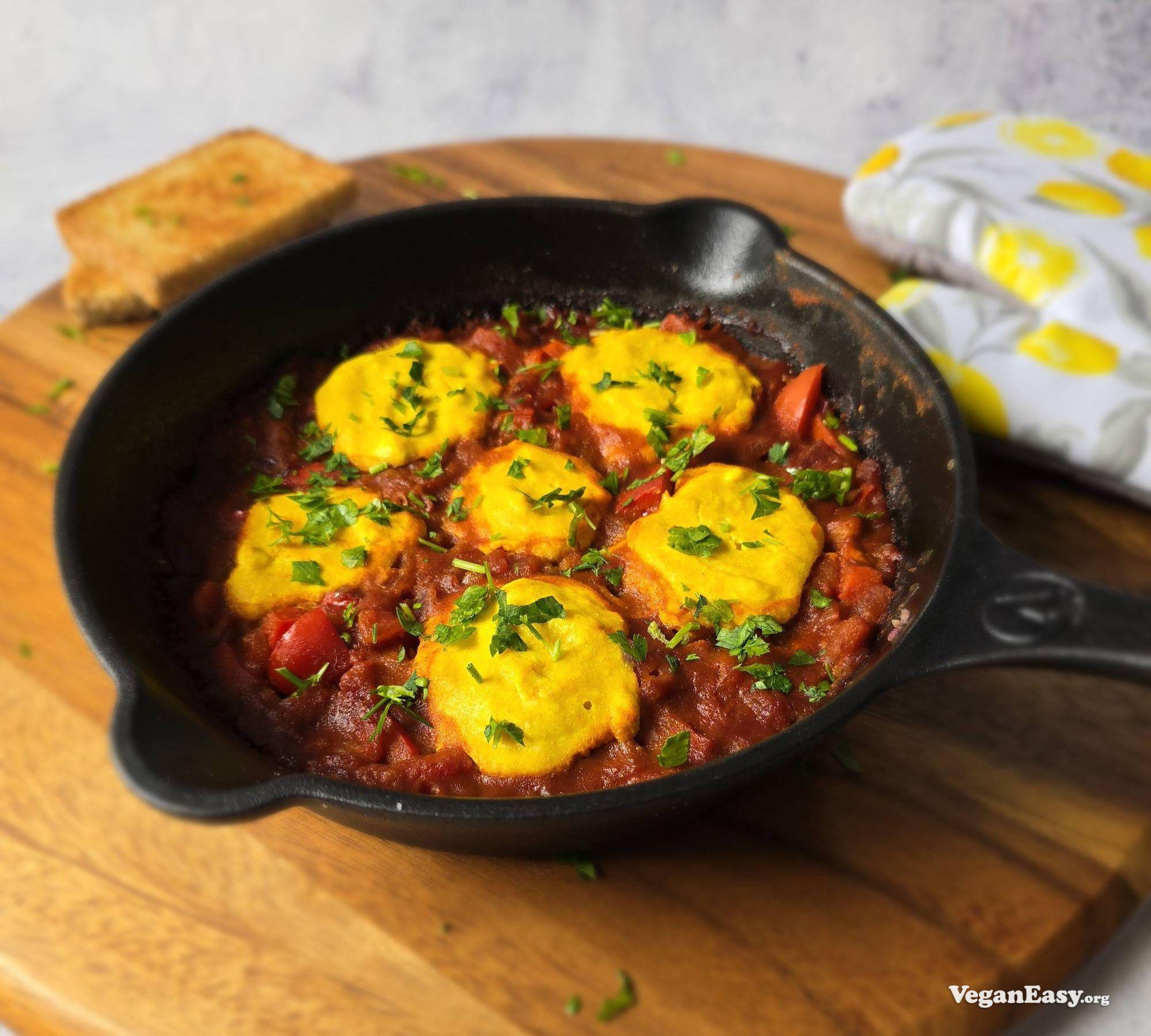 Shakshuka made with silken tofu, in a skillet sitting on top of a wooden chopping board.